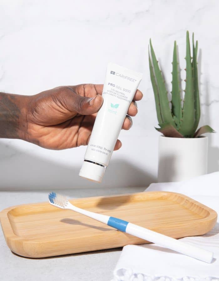 Hand holding a tube of hydroxyapatite toothpaste above a toothbrush